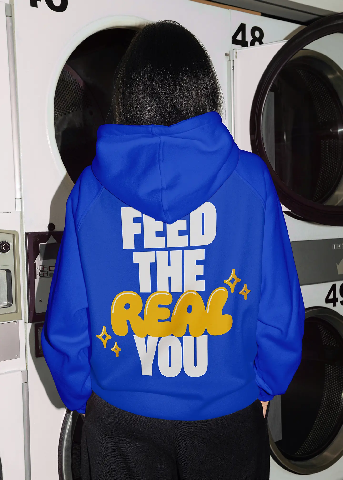 blue hoodie worn by female, with feed the real you printed on back