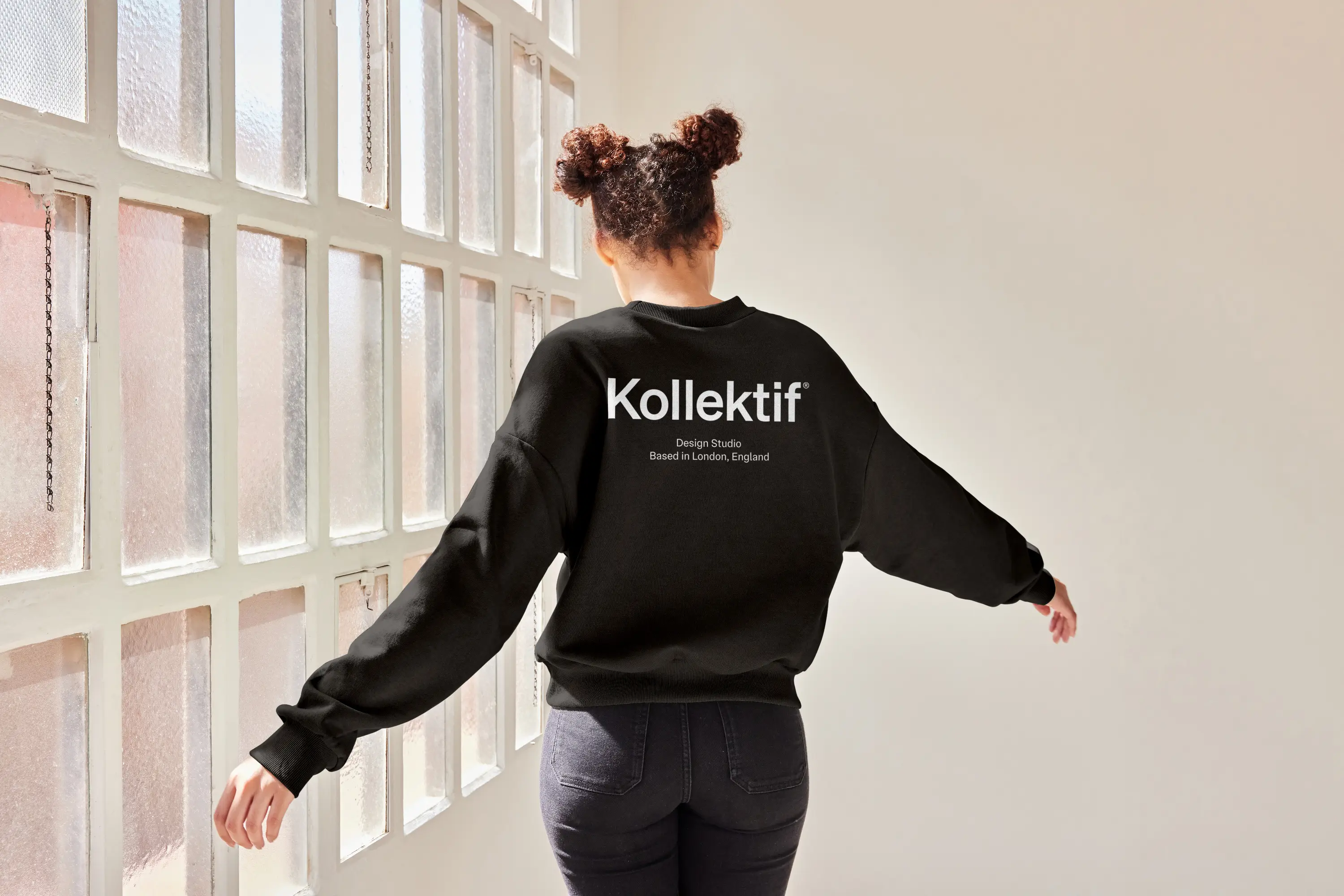 woman in studio wearing black kollektif crew neck sweater, back facing camera, arms out, kollektif logo on back