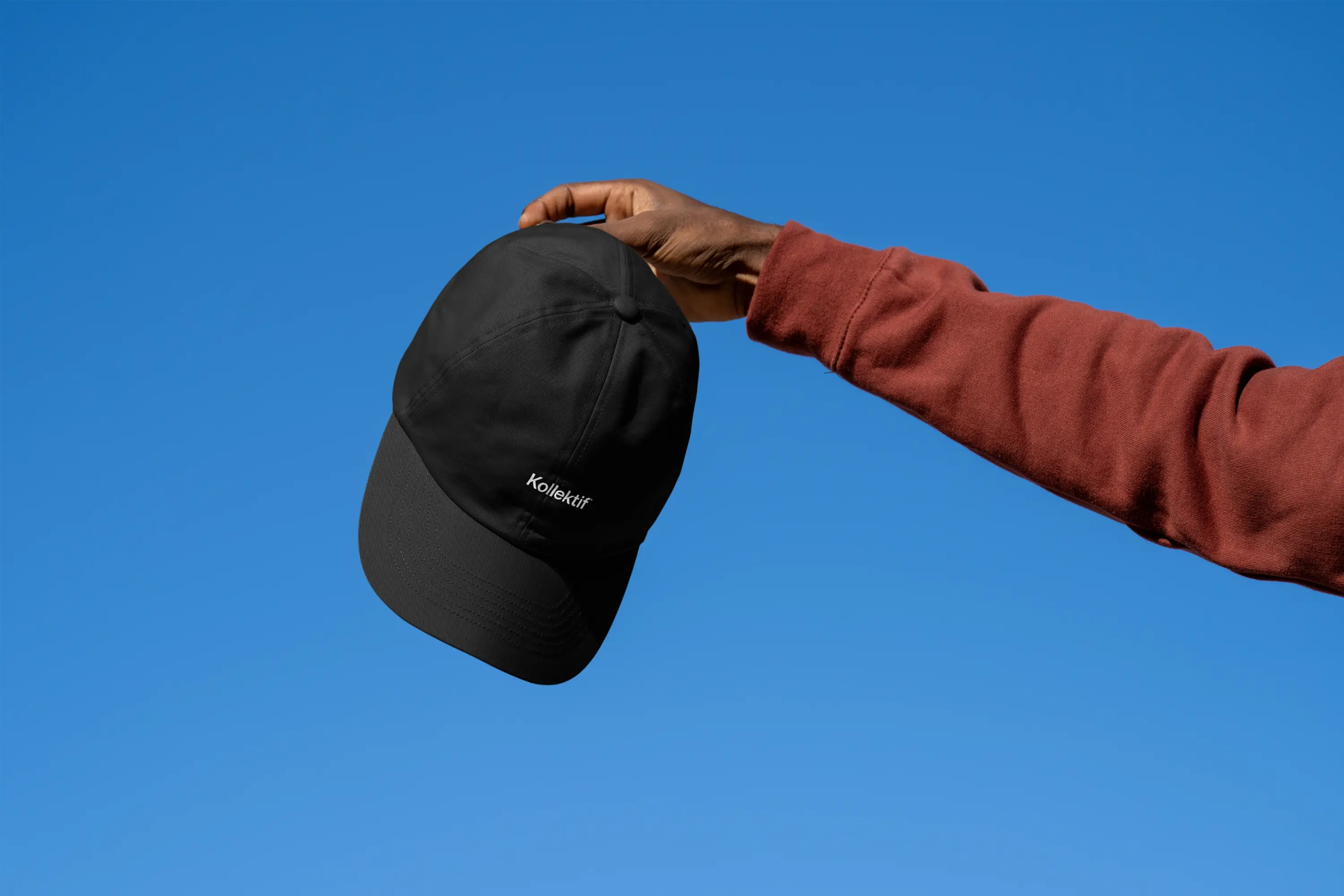 person holding black kollektif hat in the air with sky background